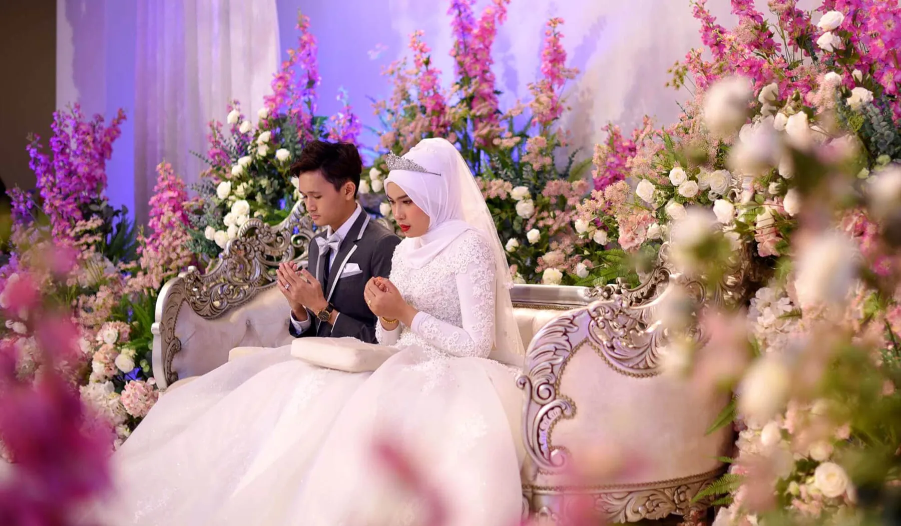 Pengantin di atas pelamin bunga bersama pasangan